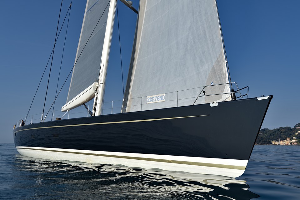 Dark-hulled sailing yacht close-hauled under a blue sky