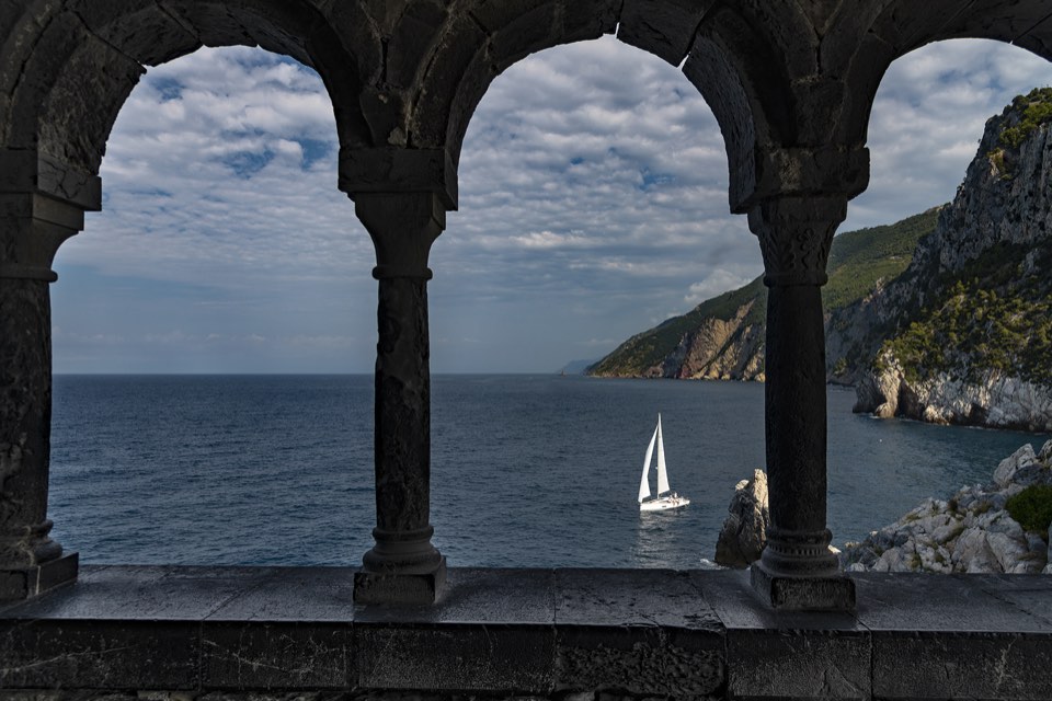 Sailing yacht seen through stone arches above the sea